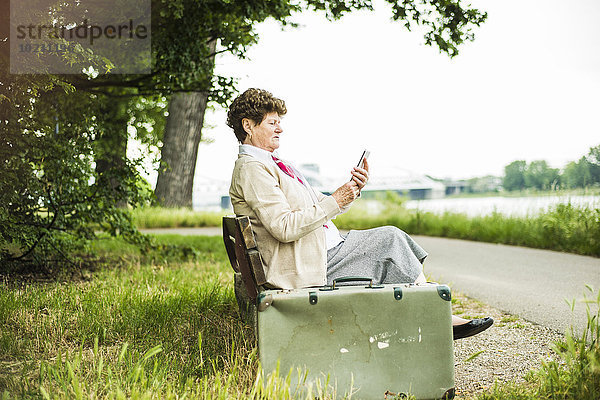 Seniorin auf der Bank sitzend mit Phablet