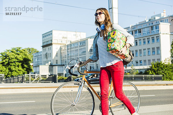 Junge Frau mit Fahrrad auf dem Bürgersteig mit Geschenkbox