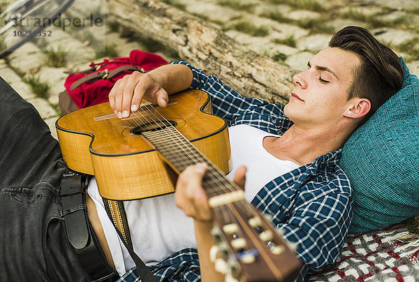 Entspannter junger Mann beim Gitarrespielen im Freien