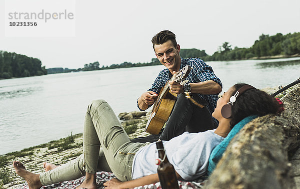 Entspanntes junges Paar mit Gitarre am Flussufer