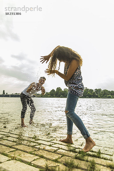 Verspieltes junges Paar  das mit Wasser am Flussufer plätschert.