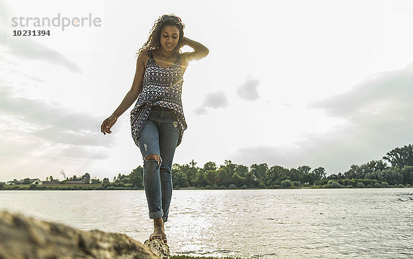 Junge Frau beim Balancieren auf dem Baumstamm am Flussufer
