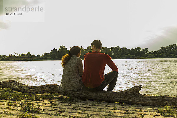 Junges Paar auf einem Baumstamm am Flussufer sitzend