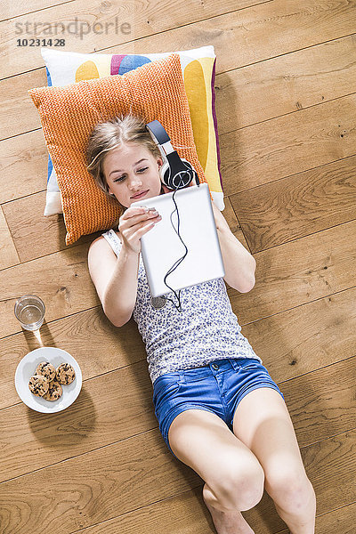 Teenager-Mädchen liegt auf dem Boden und hört Musik vom digitalen Tablett.