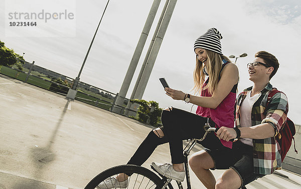 Glückliches junges Paar mit Handy zusammen auf dem Fahrrad