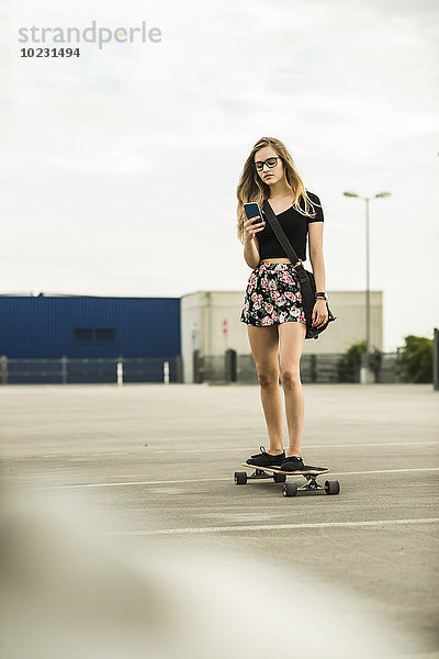 Teenager-Mädchen beim Skateboardfahren auf dem Handy