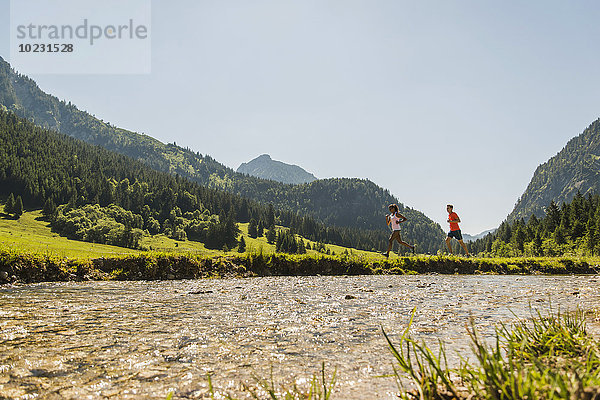Österreich  Tirol  Tannheimer Tal  junges Paar joggen am Flussufer