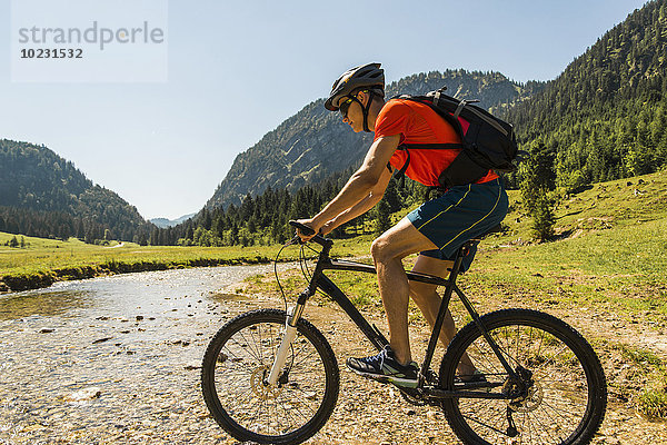 Österreich  Tirol  Tannheimer Tal  junger Mann auf dem Mountainbike überquert Bach