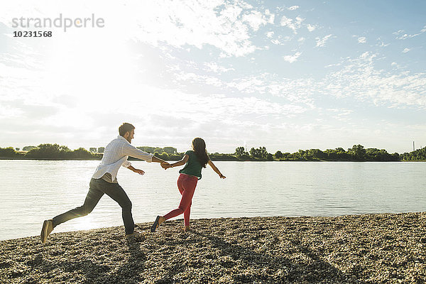 Junges Paar läuft Hand in Hand am Flussufer entlang
