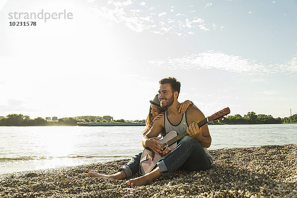 Glückliches junges Paar mit Gitarre am Flussufer