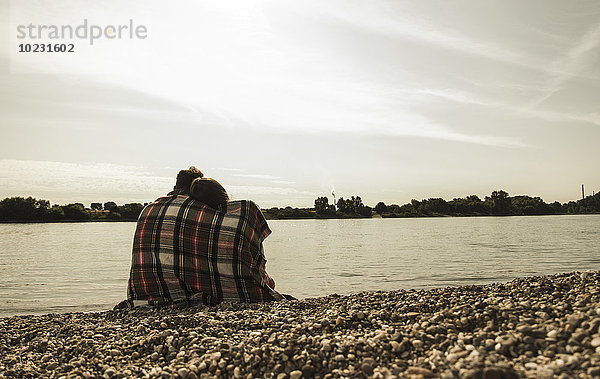 Junges Paar mit Decke am Flussufer sitzend
