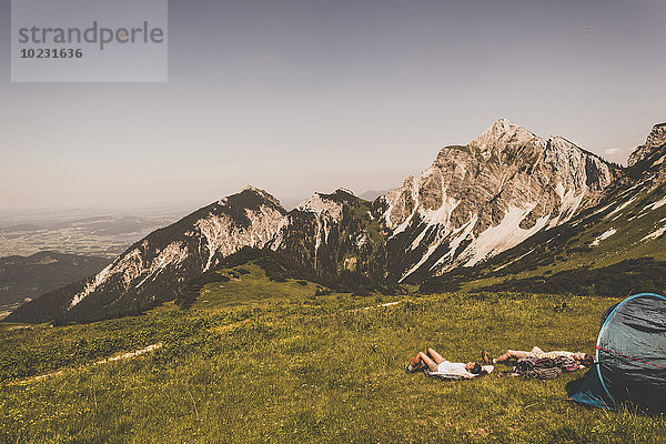 Österreich  Tirol  Tannheimer Tal  junges Paar ruht neben dem Zelt auf einer Almwiese