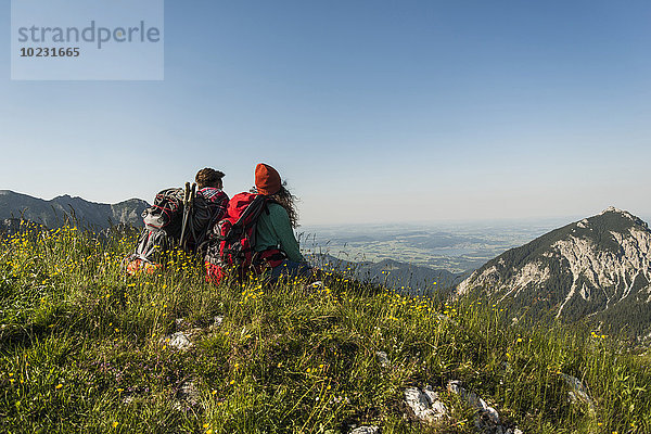 Österreich  Tirol  Tannheimer Tal  junges Paar auf der Alm sitzend mit Blick auf die Aussicht