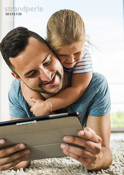 Glücklicher Vater und Tochter auf dem Teppich liegend mit digitalem Tablett