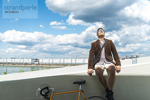 Erwachsener Mann mit Fahrrad auf der Wand sitzend und das Wetter genießend