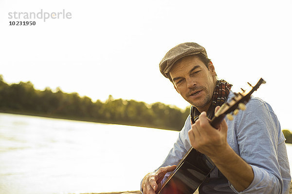 Porträt eines Mannes  der abends am Flussufer Gitarre spielt.