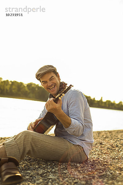 Porträt eines glücklichen Mannes  der abends am Flussufer Gitarre spielt.