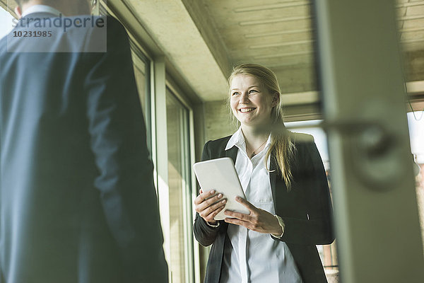 Lächelnde junge Geschäftsfrau mit digitalem Tablett beim Anblick des Geschäftsmannes