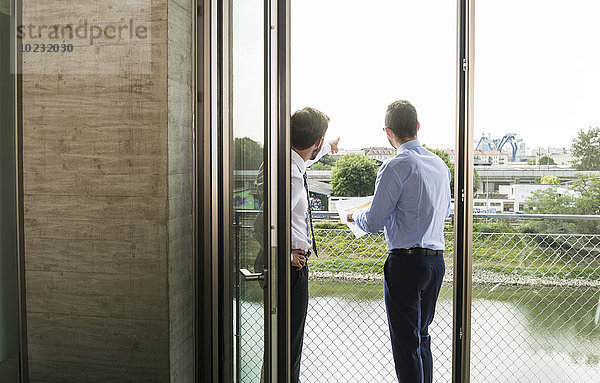 Zwei junge Geschäftsleute  die auf dem Balkon stehen und darüber diskutieren.