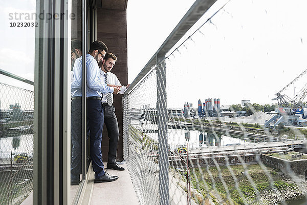 Zwei junge Geschäftsleute diskutieren über Dokumente auf dem Balkon