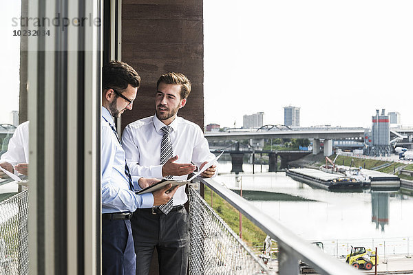 Zwei junge Geschäftsleute mit Dokumenten und digitalem Tablett diskutieren auf dem Balkon