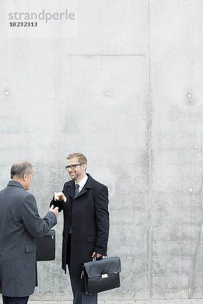 Zwei Geschäftsleute tauschen Visitenkarten an der Betonwand aus.