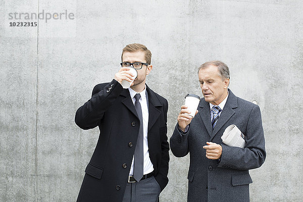 Zwei Geschäftsleute mit Kaffee an der Betonmauer