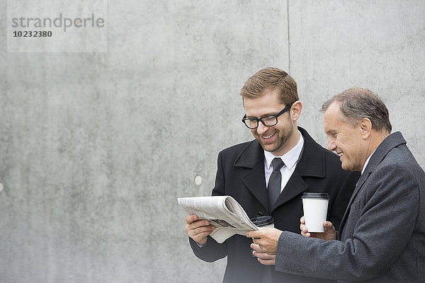 Zwei lächelnde Geschäftsleute mit Kaffee zum Mitnehmen und Zeitung