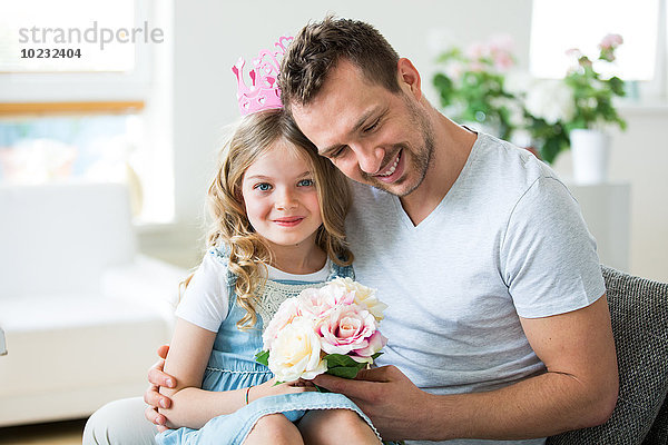 Mädchen mit rosa Krone auf Vaters Schoß sitzend mit Blumenstrauß