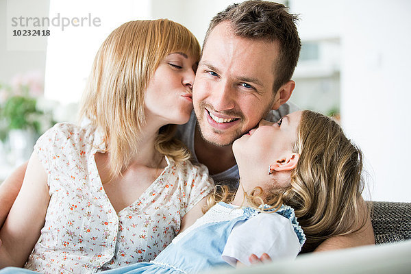 Glückliche Familie auf der Couch sitzend  Mutter und Tochter küssen Vater
