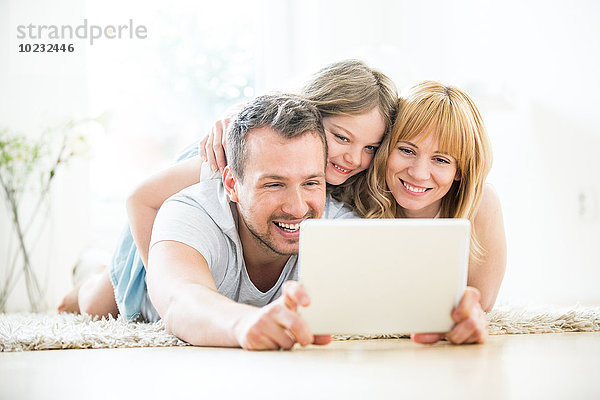Glückliche Familie auf dem Boden liegend mit digitalem Tablett