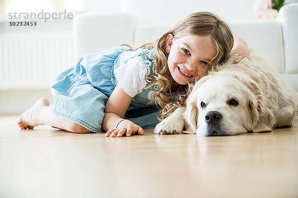 Kleines Mädchen kuschelt mit ihrem Hund  auf dem Boden liegend