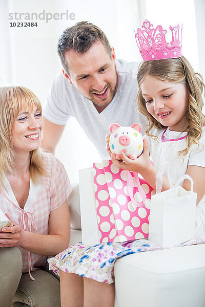 Mädchen in rosa Krone mit Geschenktüten  Eltern schauen zu
