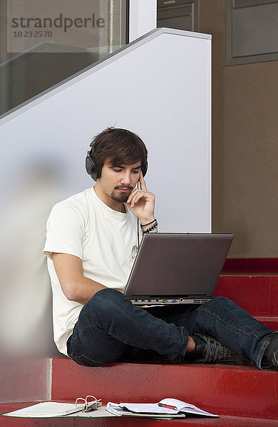 Nachdenklicher junger Mann mit Kopfhörer und Laptop