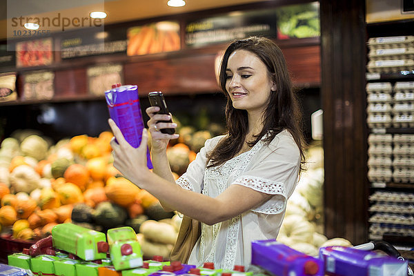 Frau im Supermarkt scannt Preise mit ihrem Smartphone