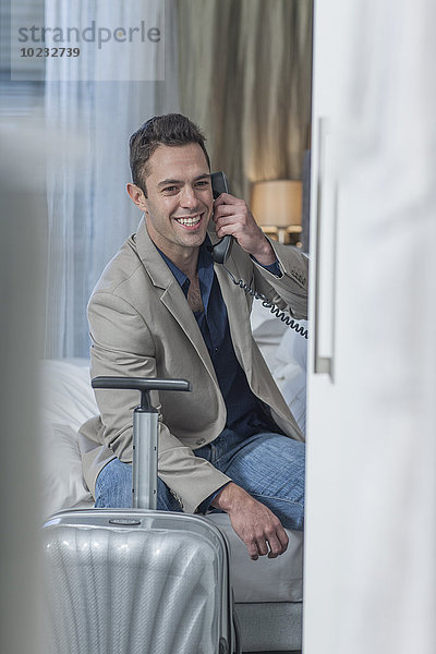 Porträt eines lächelnden Geschäftsmannes beim Telefonieren im Hotelzimmer