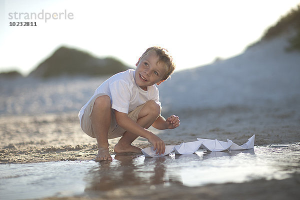 Junge spielt mit Papierbooten an einem Wasserbecken am Sandstrand