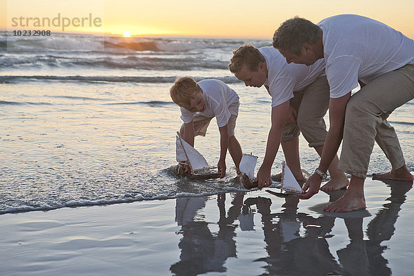 Vater und Söhne beim Spielen mit Spielzeugbooten im Wasser am Strand