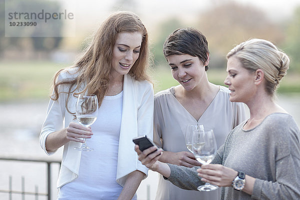 Drei Frauen mit Brille und Smartphone auf der Terrasse eines Restaurants