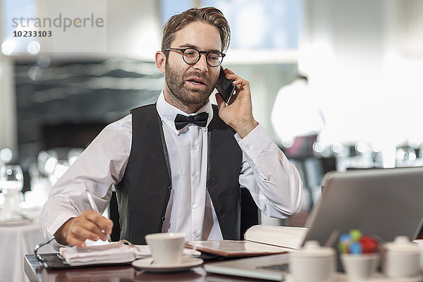 Restaurantmitarbeiter am Tisch mit Laptop und Handy