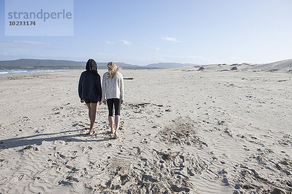 Südafrika  Kapstadt  Rückansicht von zwei jungen Frauen  die am Strand spazieren gehen