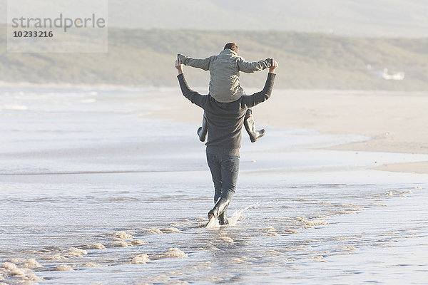 Südafrika  Kapstadt  Mann  der am Strand spazieren geht und seinen Sohn auf den Schultern trägt.