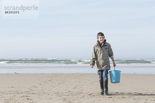 Südafrika  Witsand  Junge  der mit blauem Eimer am Strand spazieren geht
