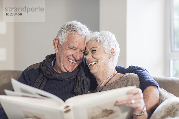 Seniorenpaar sitzend auf einer Couch mit Fotoalbum