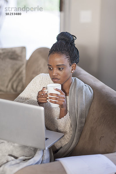 Junge Frau mit Laptop beim Kaffeetrinken zu Hause