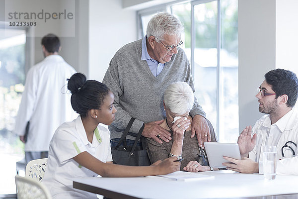 Weinende Seniorin mit Ehemann in der Klinik im Gespräch mit Arzt und Krankenschwester