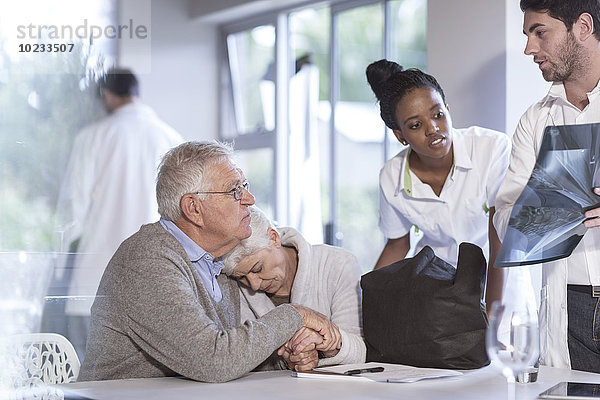 Traurige Seniorin mit Ehemann in der Klinik im Gespräch mit Arzt und Krankenschwester