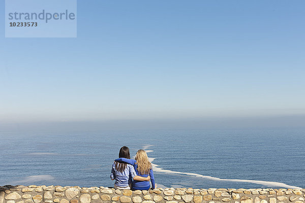 Südafrika  zwei Frauen sitzen Arm in Arm an Arm an einer Wand an der Küste