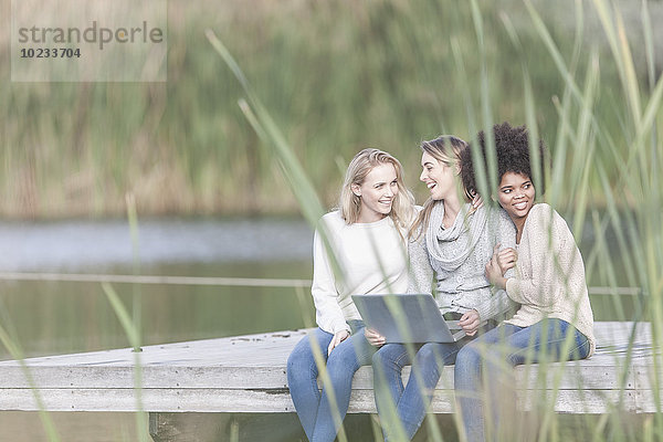 Drei Frauen mit Laptop entspannen sich an einem Steg am See