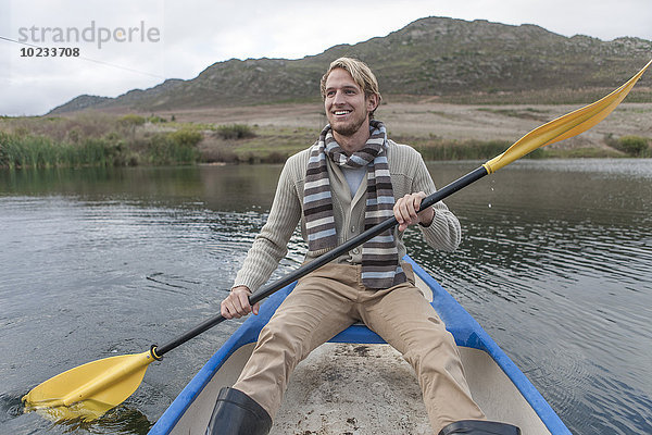 Portrait eines glücklichen jungen Mannes  der auf einem See paddelt.